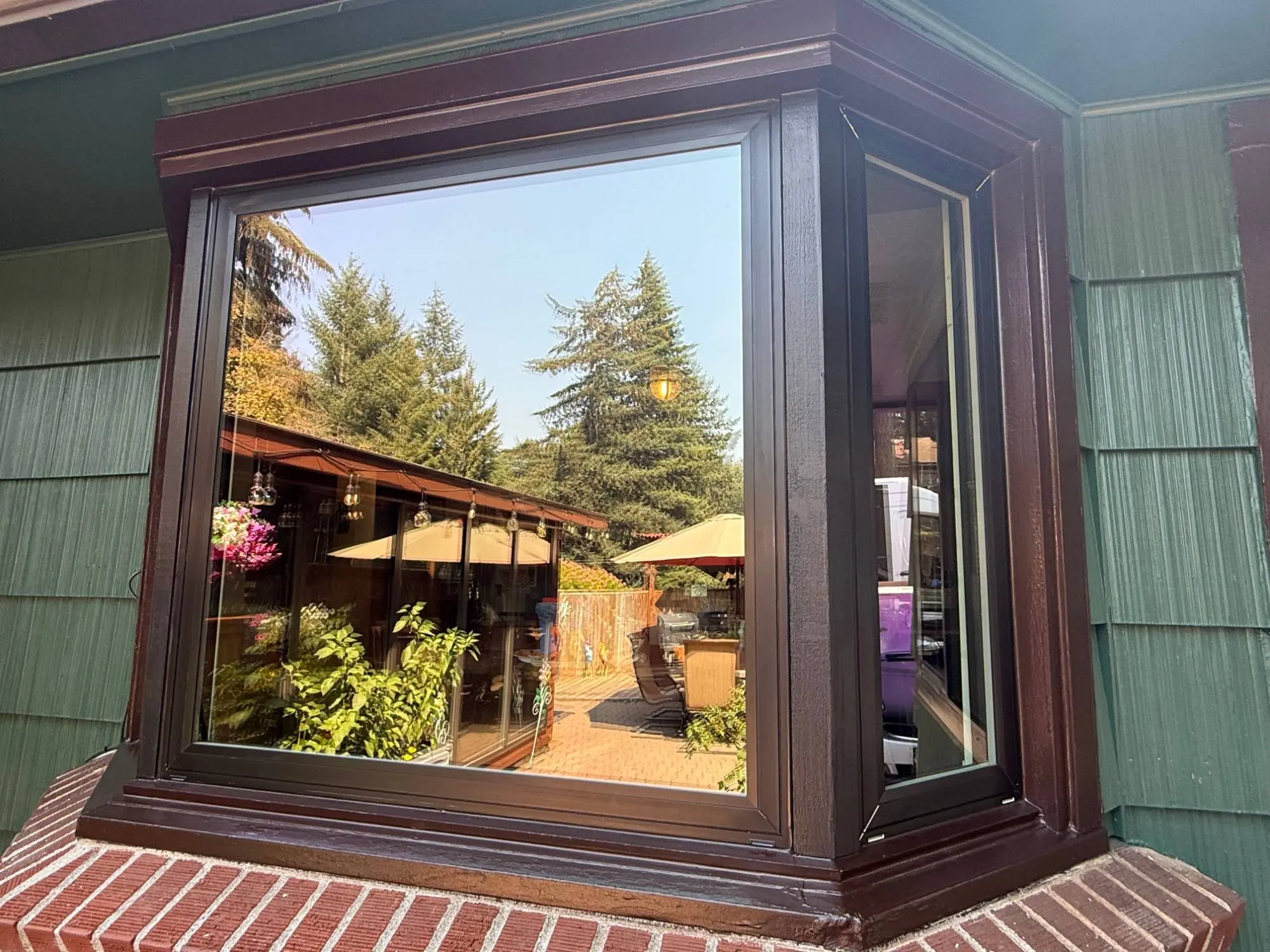 Finished bay window with new dark frames and brown trim, reflecting the backyard patio